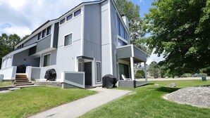 A modern two-story house with a covered porch, a small outdoor seating area, and a paved driveway. - Perfect Location at this Waterville Condo! (Waterville Valley)