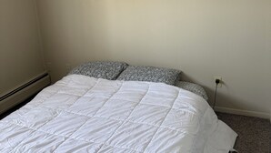 A bedroom with a white bedspread, patterned pillows, a visible electrical outlet, and a carpeted floor. - Cozy 1 bedroom in a 2 bedroom apartment in charming Mayfield Heights. (Mayfield Heights)