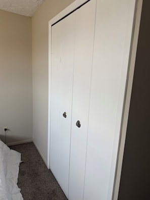 Ett vitt skåp med två dörrar och en liten hylla, ett golv täckt med matta och ett eluttag på väggen.