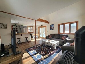 A spacious living area with a sofa, coffee table, and a grill. There is a kitchen area with a bar and stools. - Cozy Retreat in Waterville Estates! RR194E (Campton)
