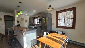 A modern kitchen with a central island, stainless steel appliances, and a dining area with a wooden table and chairs. - Cozy Retreat in Waterville Estates! RR194E (Campton)