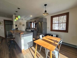 A modern kitchen with a central island, stainless steel appliances, and a dining area with a wooden table and chairs. - Cozy Retreat in Waterville Estates! RR194E (Campton)