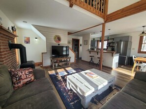 A living room with a fireplace, a television, and a kitchen in the background. - Cozy Retreat in Waterville Estates! RR194E (Campton)