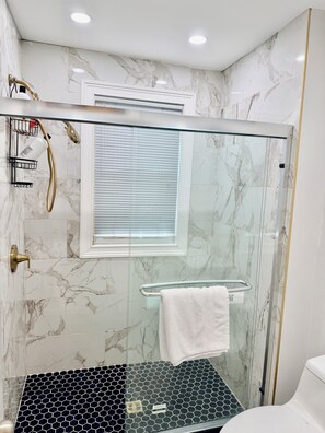 Une salle de bain moderne avec une douche à parois de verre, des murs en marbre, un sol noir à motifs hexagonaux et un porte-serviettes blanc.