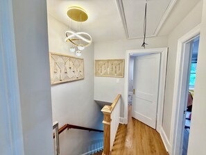 Un couloir avec un escalier en bois, une porte blanche et des panneaux décoratifs fixés au mur.