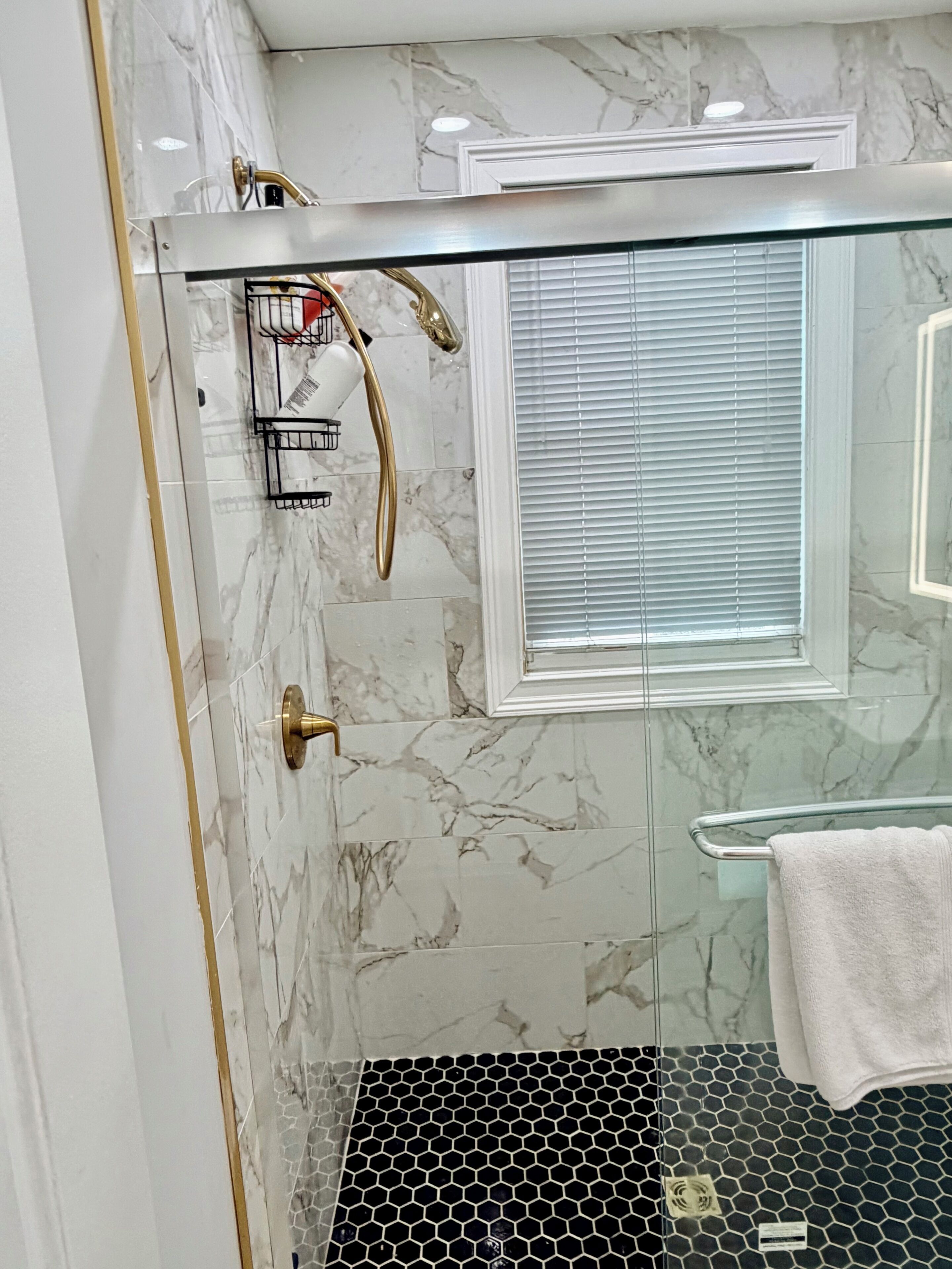Un baño moderno con cabina de ducha de vidrio, salpicadero de mármol blanco y puerta de vidrio.