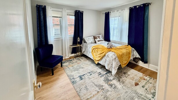 A bedroom with a bed, a chair, a bedside table, and a window with curtains.
