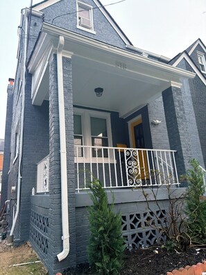 Een huis met twee verdiepingen, een veranda, een klein balkon en een schoorsteen.