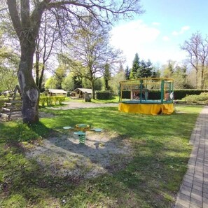 Un parc avec une aire de jeux, un arbre et un petit bâtiment.