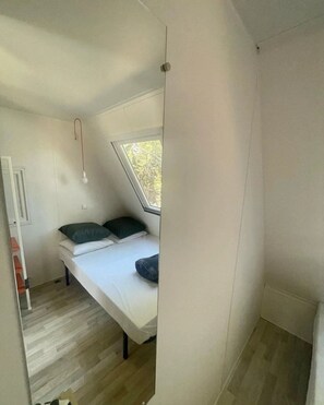 Ein kleiner, dreieckiger Raum mit einem Bett, einem Fenster und einer Tür.