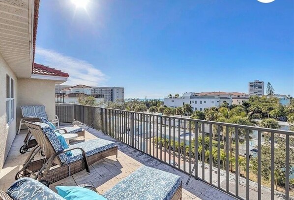 A balcony with wicker furniture, a view of the sea, and buildings in the background.