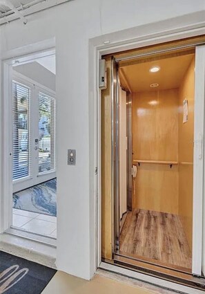 A hotel room with a wooden floor, a door with a glass panel, and a visible light switch.
