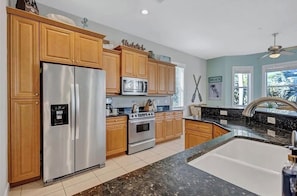 A kitchen with wooden cabinets, stainless steel appliances, a granite countertop, and a window with a view of palm trees.
