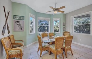 A dining area with wicker furniture, a ceiling fan, and framed pictures on the walls.