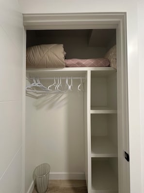 A closet with hanging space, shelves, and a small trash bin. - Cozy basement suit in Rosewood near Costco, Saskatoon (Saskatoon, SK)