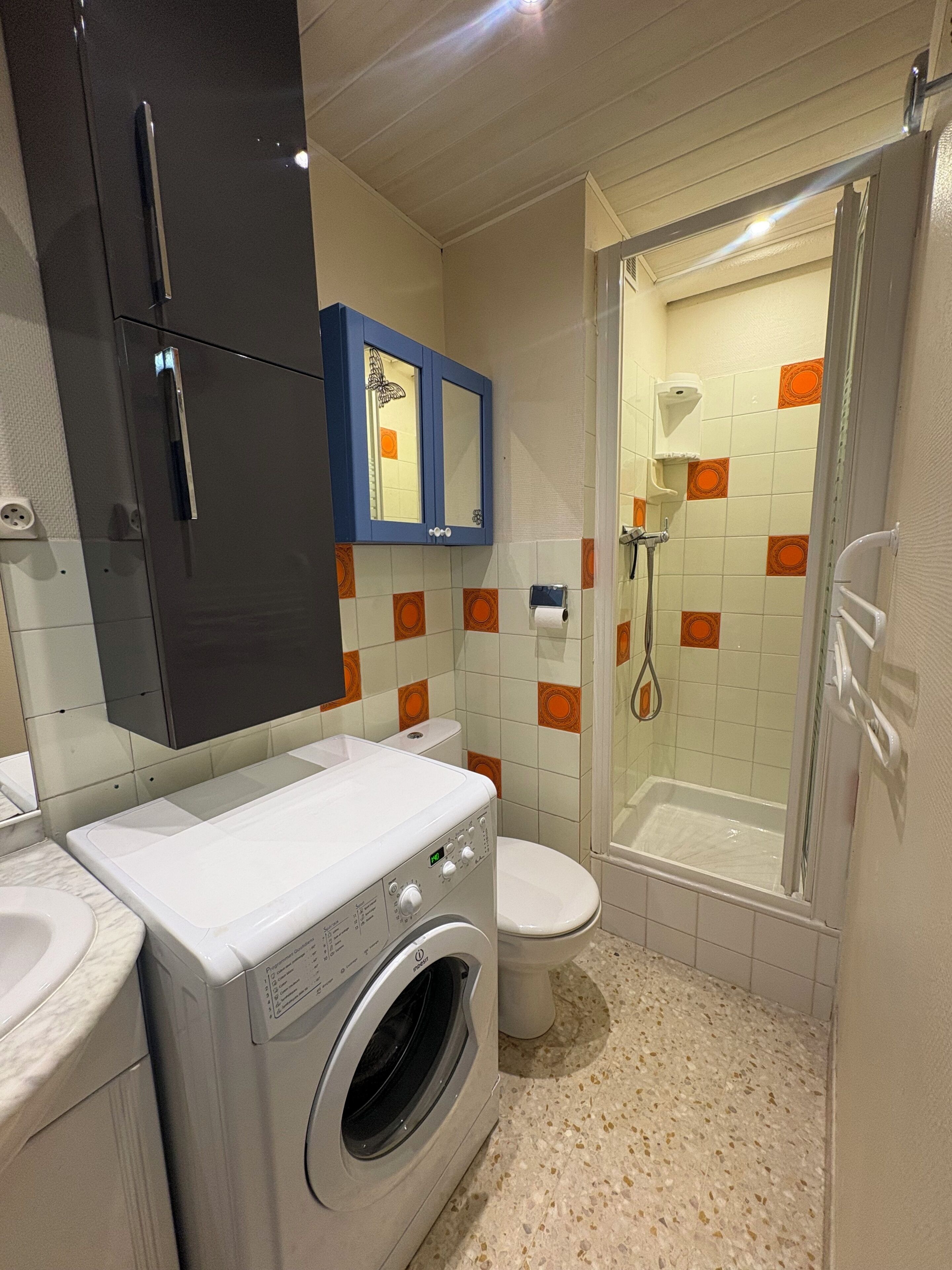 A compact bathroom with a washing machine, toilet, and shower.