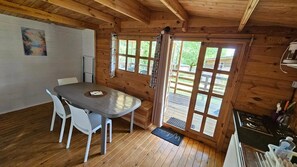 Et interiør af en træhytte med spisebord, stole, et køkken og en stor skydedør til terrassen.