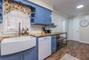 Una cocina con armarios azules, un lavamanos blanco, encimera de madera y un reloj en la pared.