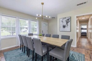 Comedor con mesa de madera y sillas grises, una araña y un cuadro de un caballo en la pared.