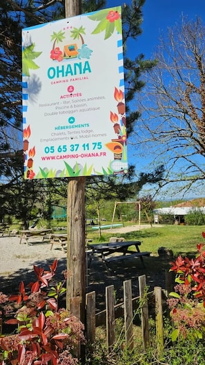 A signboard for Ohana Camping Familial with amenities like a restaurant, swimming pool, and accommodation options.