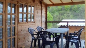A wooden cabin with a covered patio, a table with chairs, and a view of greenery. - ZEcamping 3* pataugeoire piscine chalet 29m2 5 pers (Saint-Projet)