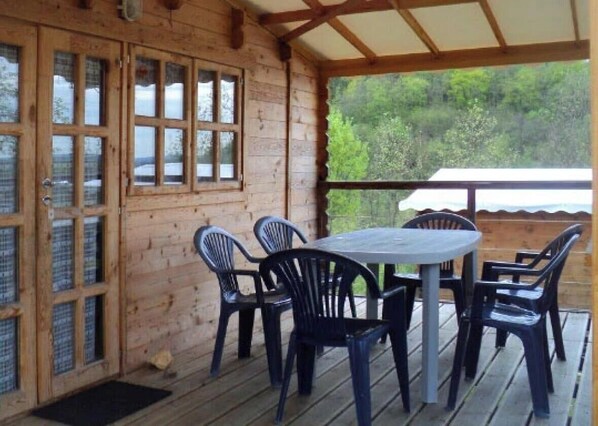 A wooden cabin with a covered patio, a table with chairs, and a view of greenery.