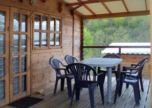 Une cabane en bois dotĂ©e dâun patio couvert, dâune table avec des chaises et offrant une vue sur la verdure.