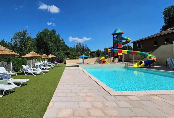 Une piscine avec un toboggan coloré, des chaises longues et des parasols.