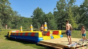 A grassy area with a colorful inflatable structure and a wooden platform. - ZEcamping 3* pataugeoire piscine chalet 29m2 5 pers (Saint-Projet)