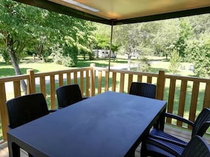 A covered outdoor patio with a table and chairs, surrounded by a wooden railing, overlooking a green landscape with trees and a clear sky. - ZEcamping 3* calme et nature - proche châteaux de la Loire (Savigny-en-Véron)