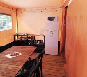A compact kitchen with a wooden table, chairs, a microwave, and a refrigerator. - ZEcamping 3* calme et nature - proche châteaux de la Loire (Savigny-en-Véron)