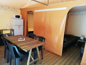 Eine Zelthütte mit Holztisch, Stühlen, Kühlschrank und einem Bett.
