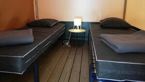 Una habitación con dos camas, una mesita con una lámpara y suelo de madera.
