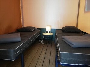Ein Zimmer mit zwei Betten, einem kleinen Tisch mit Lampe und Holzboden.