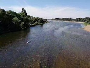Ein Fluss mit einer Person auf einem Stand-Up-Paddleboard, umgeben von Grünpflanzen und einer fernen Uferlinie.