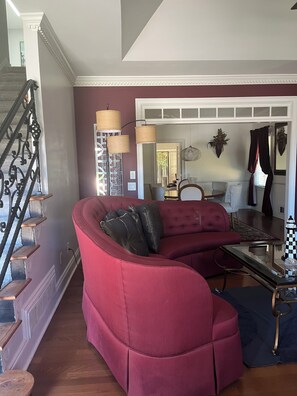 A living room with a red sofa, a staircase, and a dining area with a chandelier.
