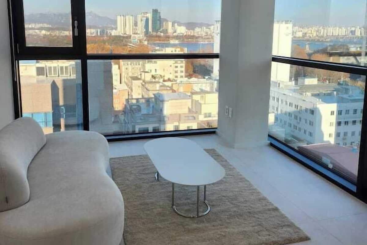 Una sala de estar moderna con un sofá, una mesita y ventanas amplias con vistas a la ciudad.