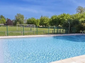 Piscina com cerca verde, árvores e céu claro.