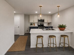 A modern kitchen with white cabinets, a marble island, stainless steel appliances, and gold bar stools. - Spacious 5-bedroom house in quaint Abilene with High-speed Internet (Abilene)