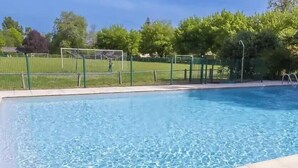 Ein Schwimmbad mit grünem Zaun, Bäumen und blauem Himmel.