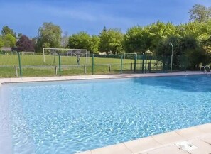 Ein Schwimmbad mit grünem Zaun, Bäumen und blauem Himmel.