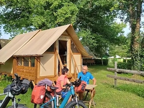Ein Zelt mit Holzgestell und Leinwanddach, ein Fahrrad und eine Person, die an einem Tisch sitzt.