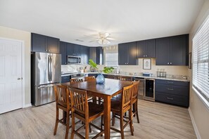 Une cuisine moderne avec des meubles de couleur sombre, des appareils en acier inoxydable, une table à manger en bois et un ventilateur de plafond.