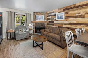 A living room with a fireplace, a sofa, a coffee table, and a dining area with chairs. - Château Rouge ~ 210 Sawmill Flats (Red Lodge)