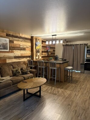 Een gezellige woonkamer met een bank, een salontafel en een eethoek met stoelen en een kleine keuken.