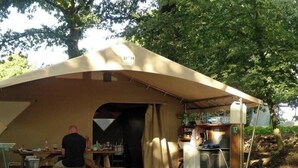 Ein Zelt mit Tisch, Stühlen, einem Kühlschrank und einer sitzenden Person am Tisch.