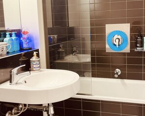 Et badeværelse med en hvid vask, en brusekabine med glasvægge og en blå, rund genstand på væggen.