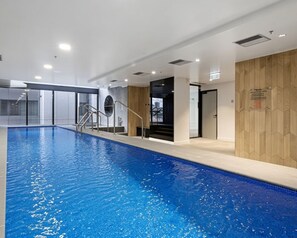 An indoor swimming pool with clear water, a metal ladder, and a wooden wall. - Free Car Space + Collins 2BR Full Apartment (West Melbourne)