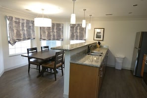 Una cocina con encimera de granito, armarios de madera, un refrigerador de acero inoxidable y una zona de comedor con mesa y sillas.
