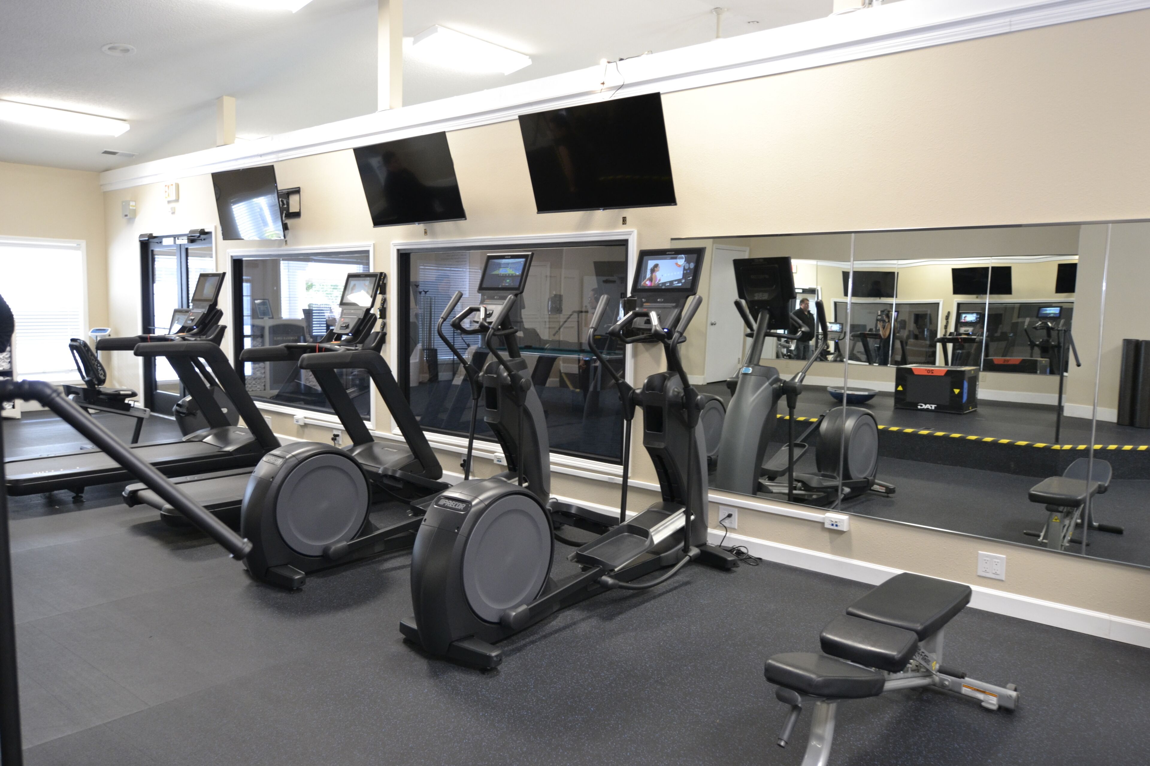 Een fitnessruimte met loopbanden, elliptische trainers en een bank.